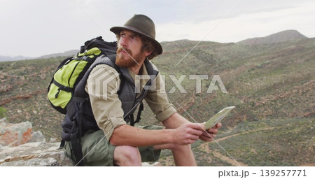 Consulting hiker with wide-brimmed hat reading paper map on cliff edge, with backpack, copy space Consulting hiker with wide-brimmed hat reading paper map on cliff edge, with backpack, copy space 139257771