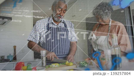 Chopping senior couple wearing aprons prepping fresh vegetables at kitchen counter, with knife Chopping senior couple wearing aprons prepping fresh vegetables at kitchen counter, with knife 139257804