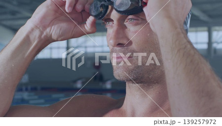 Shirtless athlete adjusting dark-tinted swim goggles in pool facility, water droplets on shoulders Shirtless athlete adjusting dark-tinted swim goggles in pool facility, water droplets on shoulders 139257972