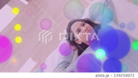 Reclining woman gazing upward on bed in bedroom at home, with pillow and abstract colored circles 139258072