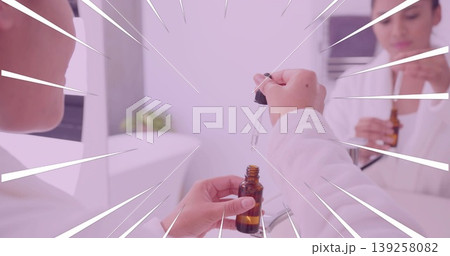 Using dropper woman in bathrobe dispensing liquid from amber bottle at vanity, reflecting in mirror 139258082