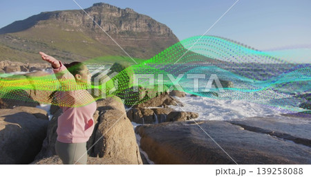 Standing Indian woman raising arms on coastal rocks, with ocean waves and digital ribbon overlay Standing Indian woman raising arms on coastal rocks, with ocean waves and digital ribbon overlay 139258088