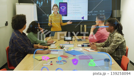 Presenting Hispanic woman in mustard sweater gesturing at conference table, with laptops and charts Presenting Hispanic woman in mustard sweater gesturing at conference table, with laptops and charts 139258094