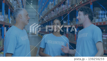Standing volunteers wearing shirts organizing cardboard boxes in warehouse, with shelving units Standing volunteers wearing shirts organizing cardboard boxes in warehouse, with shelving units 139258233