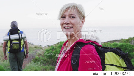 Hiking couple carrying green and black backpacks on grassy coastal trail, with silver rolled mat Hiking couple carrying green and black backpacks on grassy coastal trail, with silver rolled mat 139258270