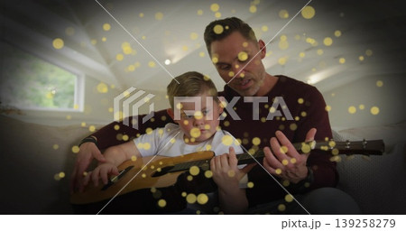 Guiding father in burgundy and son in white playing acoustic guitar on sofa, with triangular window Guiding father in burgundy and son in white playing acoustic guitar on sofa, with triangular window 139258279