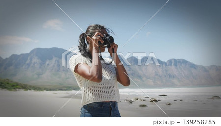 Framing photographer wearing white top and blue jeans, raising DSLR camera at shoreline with rocks Framing photographer wearing white top and blue jeans, raising DSLR camera at shoreline with rocks 139258285