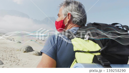 Standing man wearing red mask, blue shirt on beach with backpack and sleeping mat, copy space 139258290