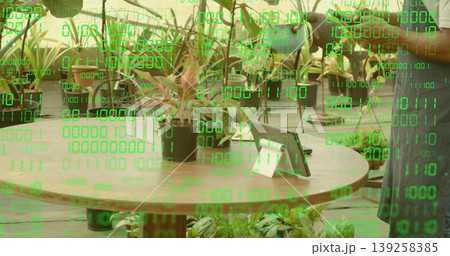 Displaying round wooden table with potted plant, tablet in nursery, with gardener watering plants Displaying round wooden table with potted plant, tablet in nursery, with gardener watering plants 139258385
