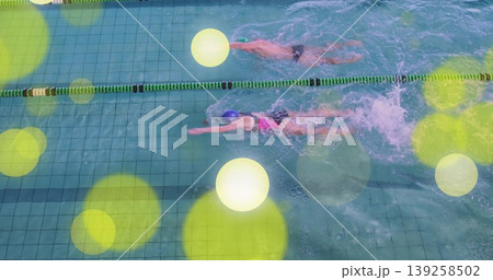 Two swimmers wearing briefs and swimsuit performing freestyle in pool, lane dividers, goggles, cap Two swimmers wearing briefs and swimsuit performing freestyle in pool, lane dividers, goggles, cap 139258502