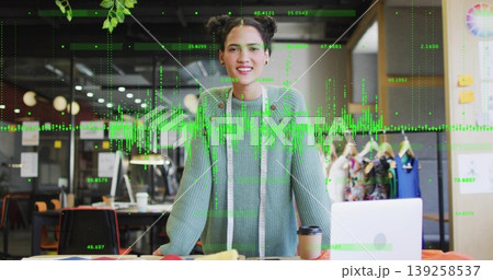 Designer in green sweater smiling and measuring fabrics in studio, with laptop and measuring tape 139258537