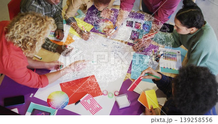 Collaborating design team leaning around table in studio, passing color wheel and paint samples Collaborating design team leaning around table in studio, passing color wheel and paint samples 139258556