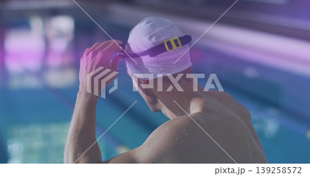 Male swimmer adjusting purple goggles with yellow clip and wearing white swim cap in lap pool Male swimmer adjusting purple goggles with yellow clip and wearing white swim cap in lap pool 139258572
