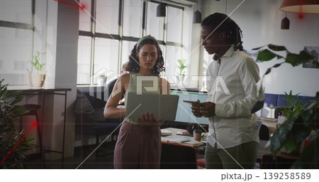 Reviewing laptop screen, two coworkers standing in open-plan office, with dual monitors, plants Reviewing laptop screen, two coworkers standing in open-plan office, with dual monitors, plants 139258589