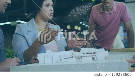 Presenting woman architect wearing blazer, gesturing with pencil at model in studio, with coworkers Presenting woman architect wearing blazer, gesturing with pencil at model in studio, with coworkers 139258600