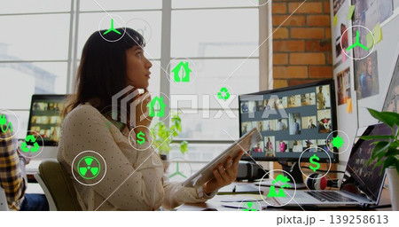 Contemplating woman in polka-dot blouse holding tablet at office desk, with pinboard and monitor 139258613