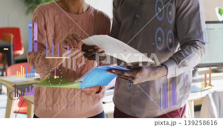 Professionals reviewing reports and color coded folders in office, with floating charts Professionals reviewing reports and color coded folders in office, with floating charts 139258616