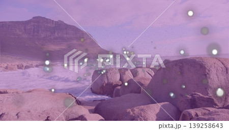 Crashing waves hitting granite boulders on shoreline, rising mountain ridge and floating light orbs Crashing waves hitting granite boulders on shoreline, rising mountain ridge and floating light orbs 139258643