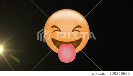 Floating yellow smiley face emoji sticking out pink tongue in black graphic space, with lens flare 139258660