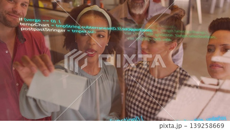 Collaborating team placing index cards on transparent board at open-plan office, with code snippets 139258669