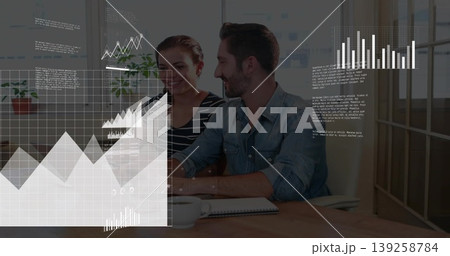 Business professionals analyzing digital charts at office desk, with notebook and white coffee cup 139258784