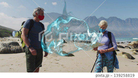 Mature couple scanning digital swirl on sandy shore with backpacks poles map and masks 139258819