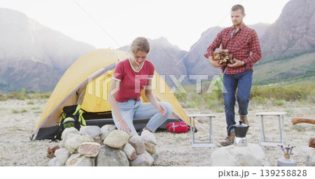 Stacking stone ring woman and carrying firewood man at mountain valley campsite, with yellow tent Stacking stone ring woman and carrying firewood man at mountain valley campsite, with yellow tent 139258828