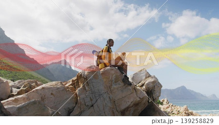Sitting hiker in yellow jacket gazing over sea on jagged rock, with red backpack, sleeping pad Sitting hiker in yellow jacket gazing over sea on jagged rock, with red backpack, sleeping pad 139258829