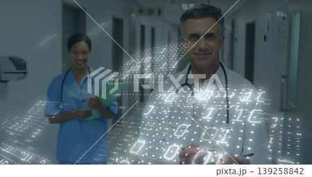 Interacting mature male doctor using interface in hospital hallway, with tablet stylus, copy space 139258842