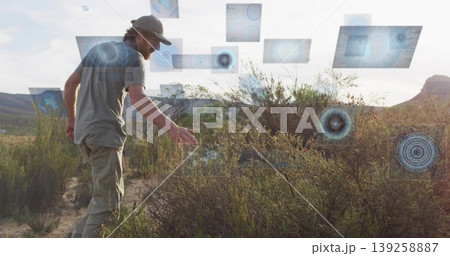 Analyzing man wearing baseball cap reaching toward shrubs with digital panels in desert, copy space Analyzing man wearing baseball cap reaching toward shrubs with digital panels in desert, copy space 139258887