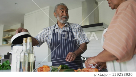 Senior couple in aprons lifting rice cooker lid slicing carrots on cutting board at kitchen island 139258920