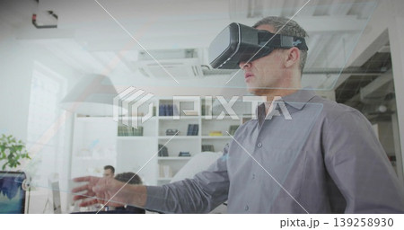 Standing mature White man wearing virtual reality headset reaching in open office, with computers 139258930