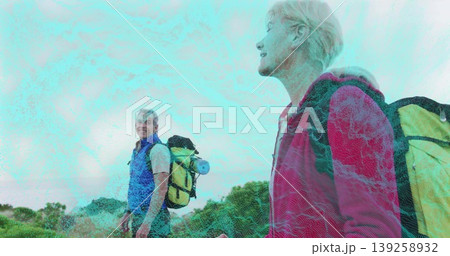 Walking couple wearing red jacket, blue vest on mountainous hillside trail, with backpacks 139258932