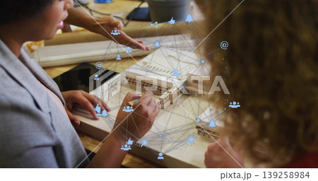 Collaborating designers wearing blazers sketching wooden scale model in studio, with overlay icons Collaborating designers wearing blazers sketching wooden scale model in studio, with overlay icons 139258984