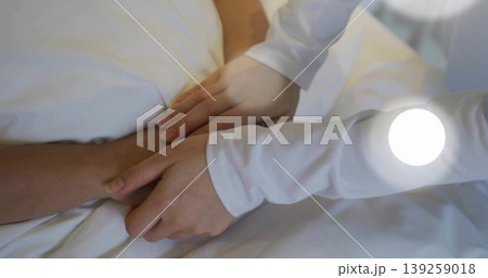 Offering comfort by daughter placing hands on father's forearm in bedroom with white bed sheets Offering comfort by daughter placing hands on father's forearm in bedroom with white bed sheets 139259018
