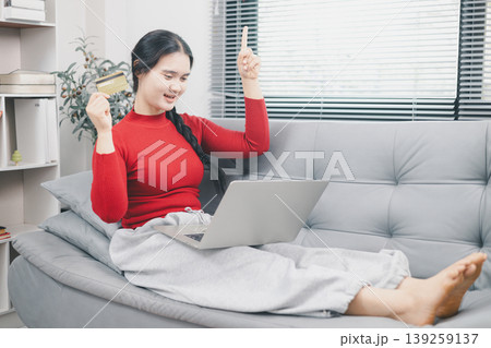 Young Asian woman celebrating online shopping success with laptop and credit card at home, pointing up for sale or cashback offer, ecommerce payment, discount deal and digital purchase concept Young Asian woman celebrating online shopping success with laptop and credit card at home, pointing up for sale or cashback offer, ecommerce payment, discount deal and digital purchase concept 139259137