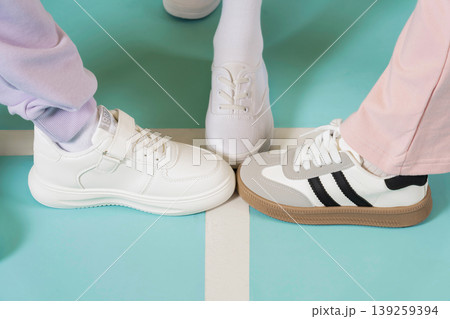 Three pairs of shoes meet on a bright floor. Each person wears different styles of shoes. The setting looks fun and casual for a social moment among friends. Three pairs of shoes meet on a bright floor. Each person wears different styles of shoes. The setting looks fun and casual for a social moment among friends. 139259394