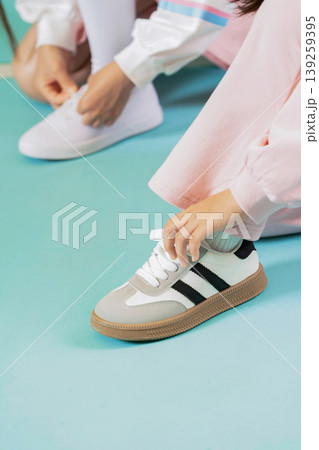 One person is tying the laces of their shoes on a blue floor. Another person sits nearby and is getting ready to put on white sneakers. Both individuals are engaged in their activity. One person is tying the laces of their shoes on a blue floor. Another person sits nearby and is getting ready to put on white sneakers. Both individuals are engaged in their activity. 139259395