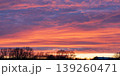 Vibrant sunset sky with layered colorful clouds over rural tree silhouettes 139260471