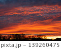 Fiery sunset sky with dramatic orange and red clouds over dark trees 139260475