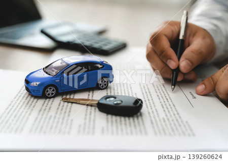 Hand holding pen signing car loan finance document contract with blue toy car model and key on paperwork, representing auto finance agreement approval, vehicle lease purchase, loan application process Hand holding pen signing car loan finance document contract with blue toy car model and key on paperwork, representing auto finance agreement approval, vehicle lease purchase, loan application process 139260624