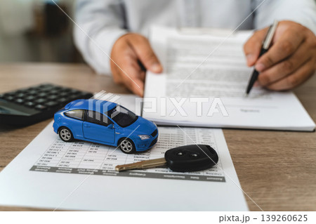 Hands reviewing car loan finance document contract with payment schedule table, blue toy car model and key on paperwork, calculator on desk, representing auto finance agreement analysis, vehicle lease Hands reviewing car loan finance document contract with payment schedule table, blue toy car model and key on paperwork, calculator on desk, representing auto finance agreement analysis, vehicle lease 139260625