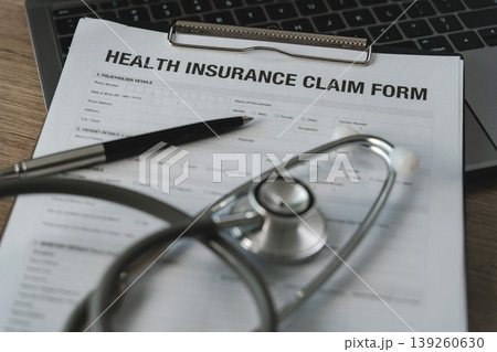 Health insurance claim and medical coverage concept with claim form, stethoscope, and pen on clipboard over laptop keyboard, healthcare paperwork document for policy application on wooden desk. Health insurance claim and medical coverage concept with claim form, stethoscope, and pen on clipboard over laptop keyboard, healthcare paperwork document for policy application on wooden desk. 139260630