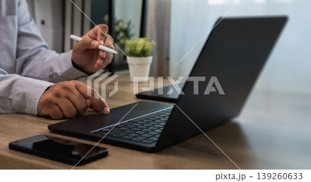 Hands using laptop keyboard and stylus on desk with smartphone and plant, interacting with touchpad and typing workflow for digital communication and online work process with copy space background. Hands using laptop keyboard and stylus on desk with smartphone and plant, interacting with touchpad and typing workflow for digital communication and online work process with copy space background. 139260633