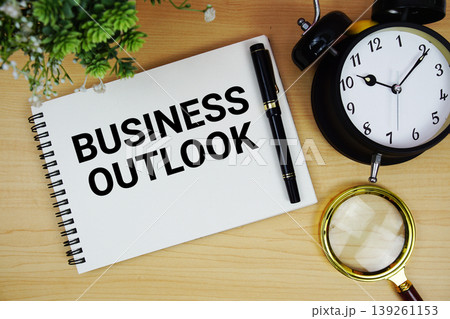 Business Outlook text written on notepad with alarm clock and magnifying glass flat lay on wooden background 139261153