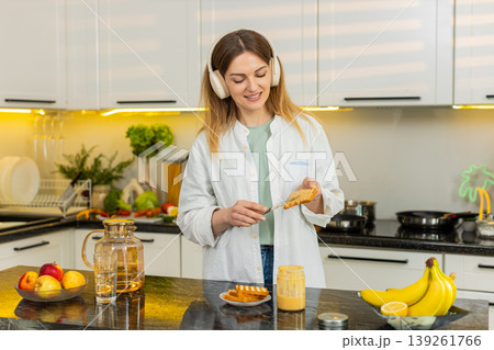 Middle-aged woman dancing to music while making healthy fresh breakfast toast in own kitchen indoors Middle-aged woman dancing to music while making healthy fresh breakfast toast in own kitchen indoors 139261766