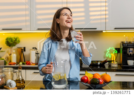 Young woman pouring cold lemon water in home kitchen to quench thirst for diet hydration fit routine Young woman pouring cold lemon water in home kitchen to quench thirst for diet hydration fit routine 139261771