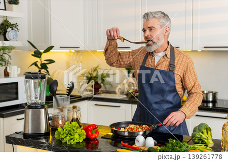 Middle-aged man seasoning tasting vegetables on electric stove in home kitchen for healthy diet meal 139261778