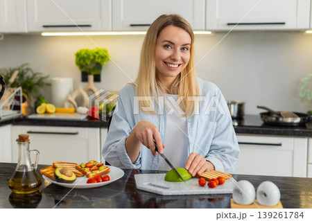 Young woman slicing avocado for tomato toast breakfast preparing healthy meal in modern home kitchen 139261784