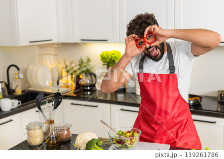 Arabian young adult man making pepper ring goggles in kitchen at home while cooking fresh keto salad Arabian young adult man making pepper ring goggles in kitchen at home while cooking fresh keto salad 139261786